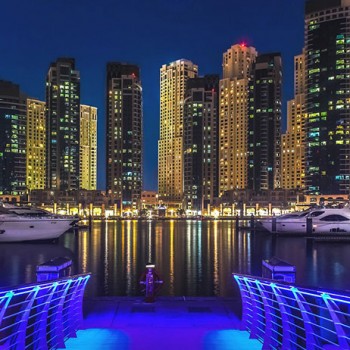 Dubai Marina éjszakai városképe, modern felhőkarcolók és jachtok a vízparton.