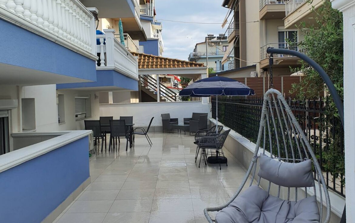 Függőszék és kültéri bútorok egy teraszon, modern épületek között.