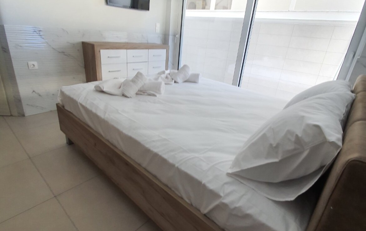 Hálószoba egy ággyal, fehér ágyneművel és tévével a falon.