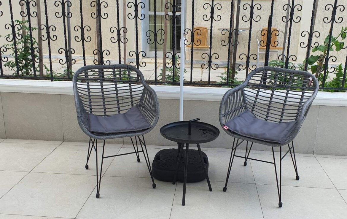 Két fekete szék és egy kék csíkos napernyő egy teraszon, mellette egy kis asztal.