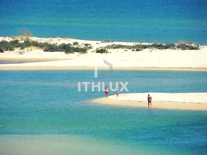 Tengerparti táj, ahol három ember fürdik a vízben, körülöttük homokos part található.