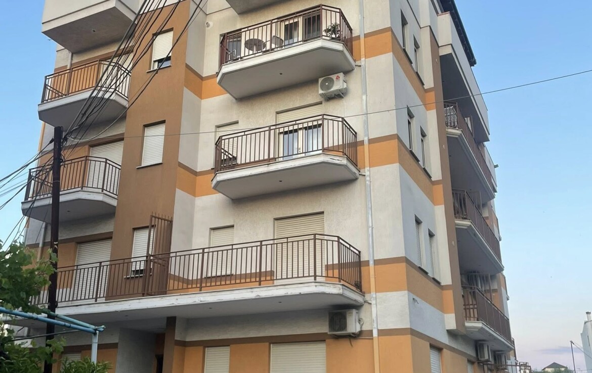 Többemeletes lakóépület erkélyekkel és autóval a parkolóban.