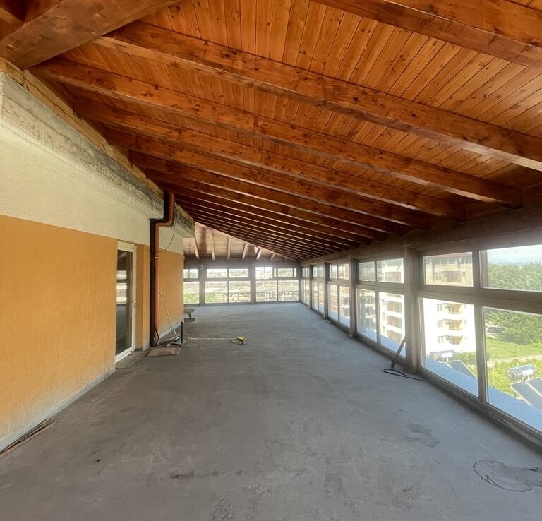 Tetőtéri ingatlan belső terének fa mennyezete és nagy ablakai láthatók.